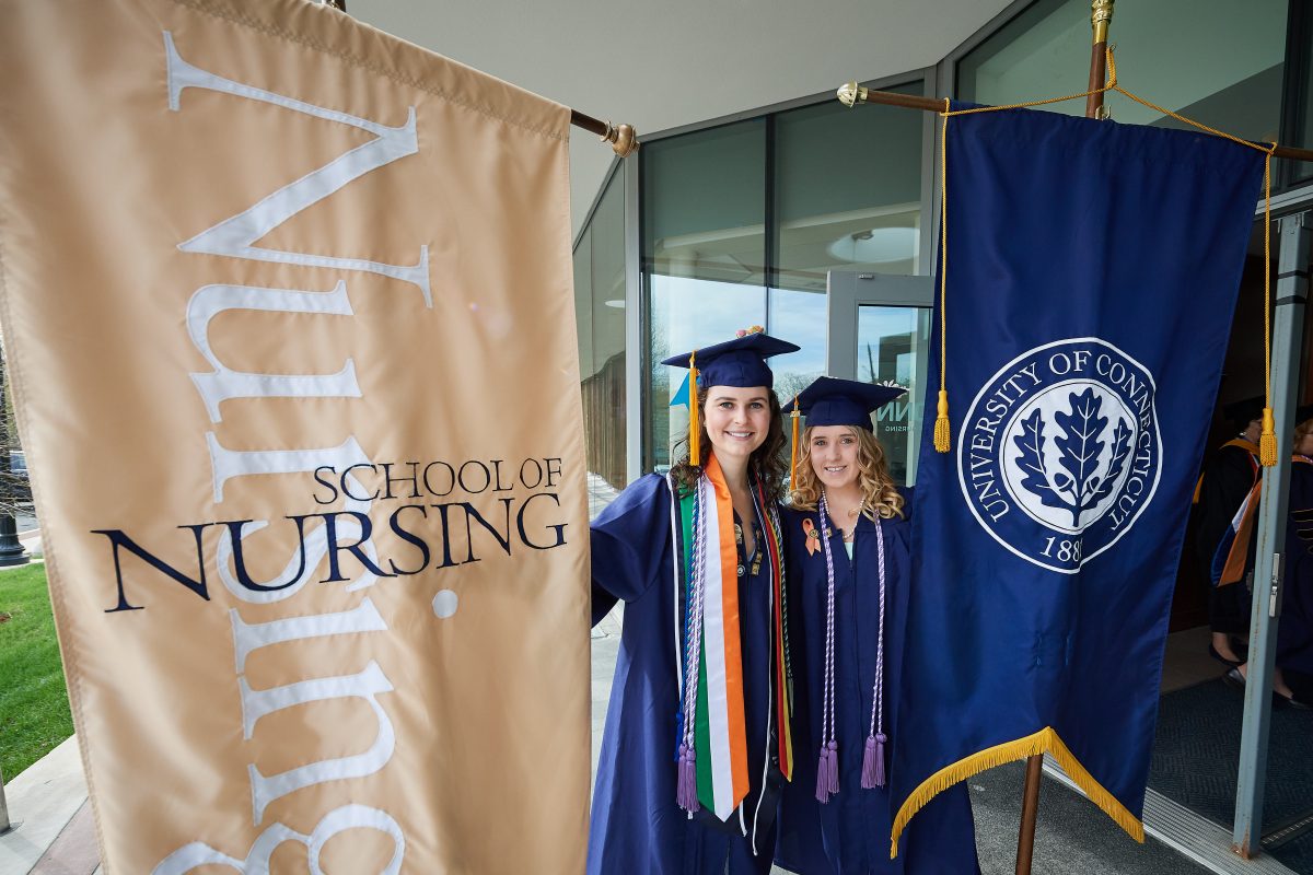 Kelly McGovern '18 (NUR), left and Taylor Varrato '18 (NUR) hold the school banners at the Carolyn Ladd Widmer Wing of Storrs Hall before start of the School of Nursing Commencement procession on May 5, 2018. (Peter Morenus/UConn Photo)